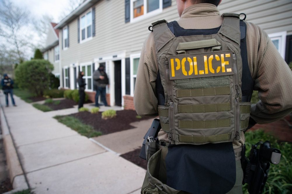 ICE ERO deportation officers in POLICE tactical vests approaching a residential home during an enforcement operation similar to the Queens raid