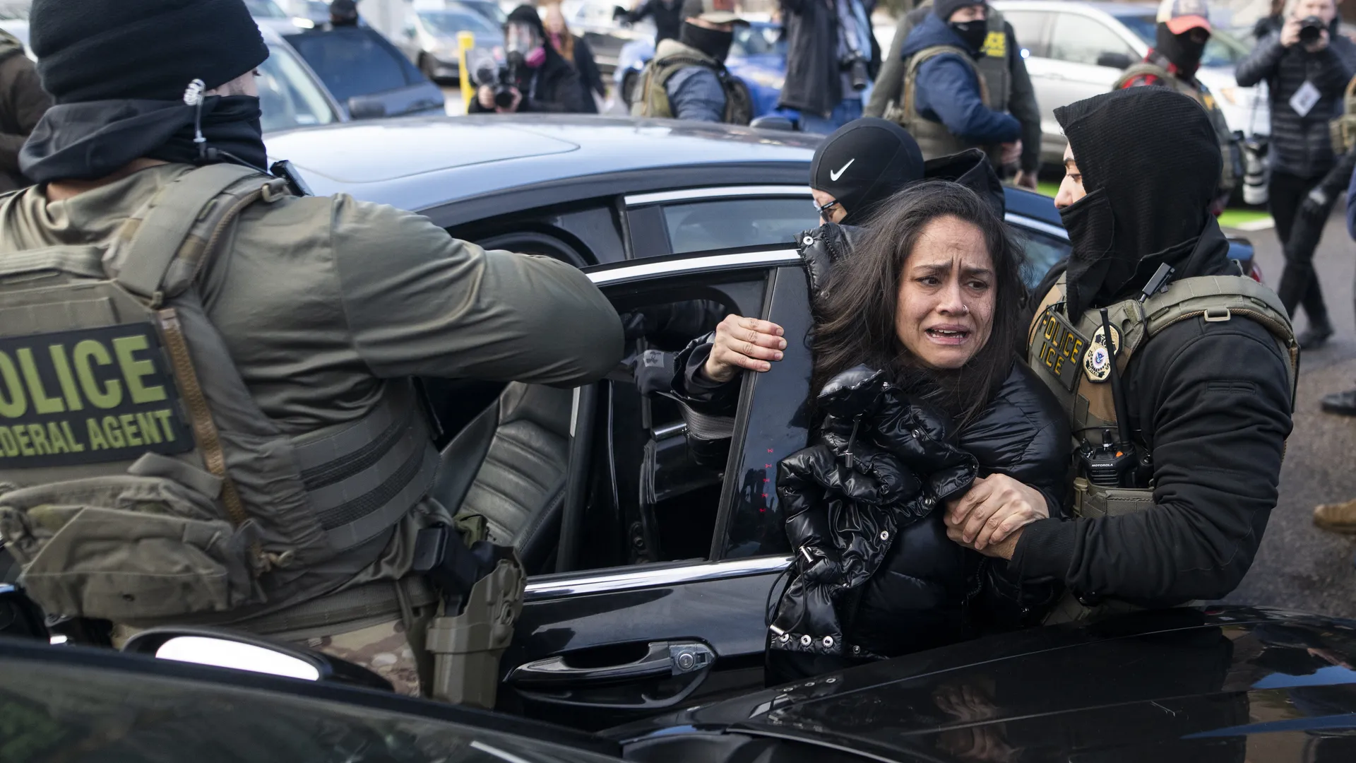 Federal agents marked POLICE FEDERAL AGENT detaining a distressed woman during a vehicle stop as bystanders observe